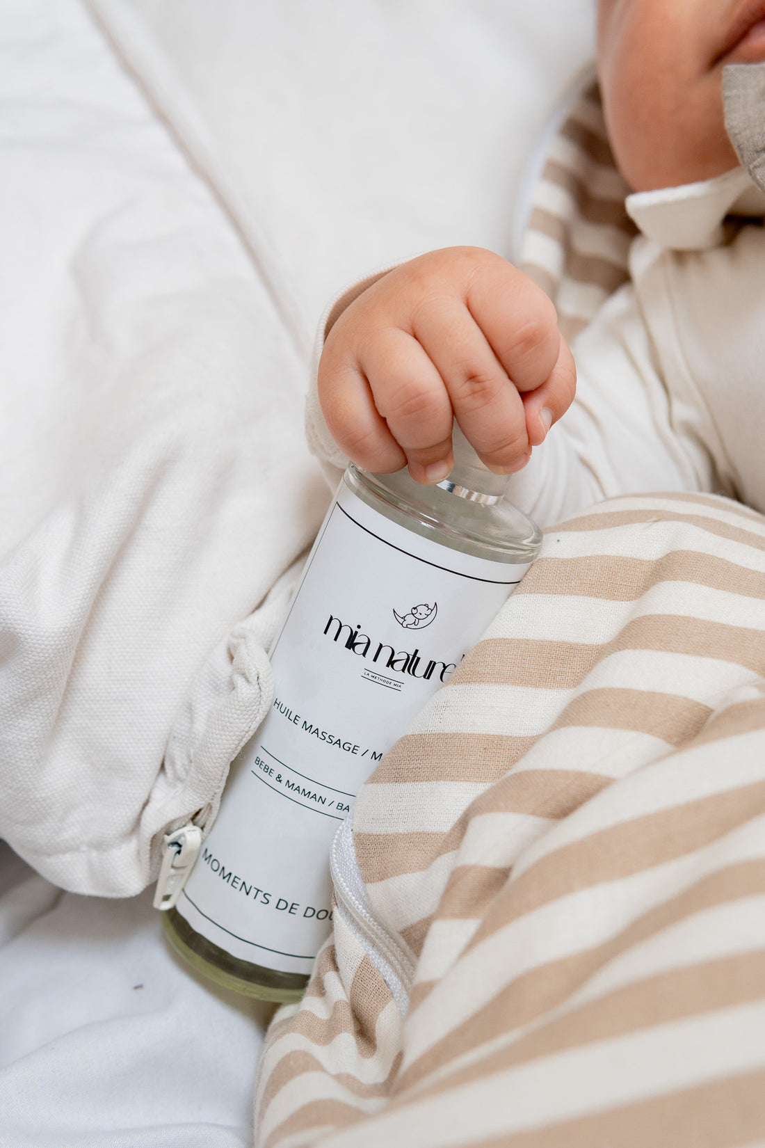 bébé qui tient une bouteille d'huile de massage nourrissante dans sa main.