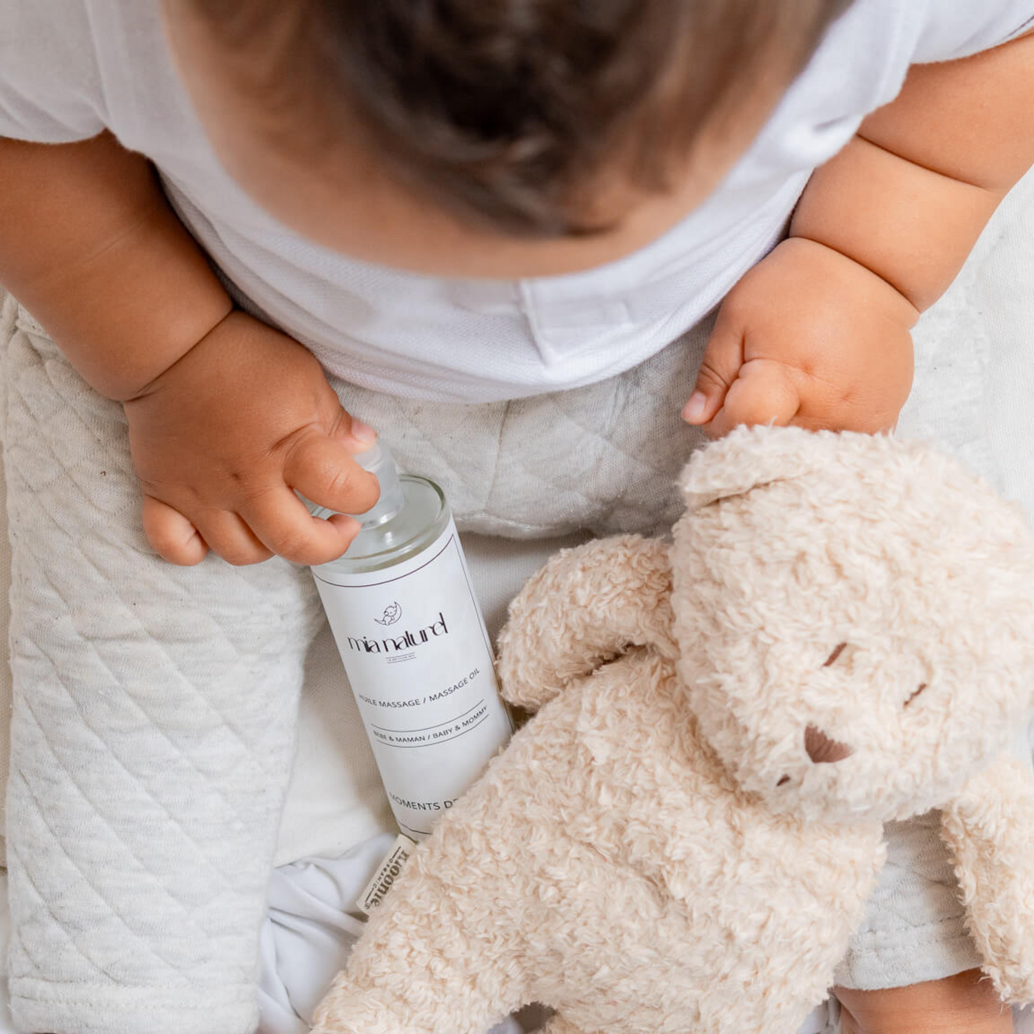 Bébé qui tient dans sa main une bouteille d'huile nourrissante pour le massage bébé